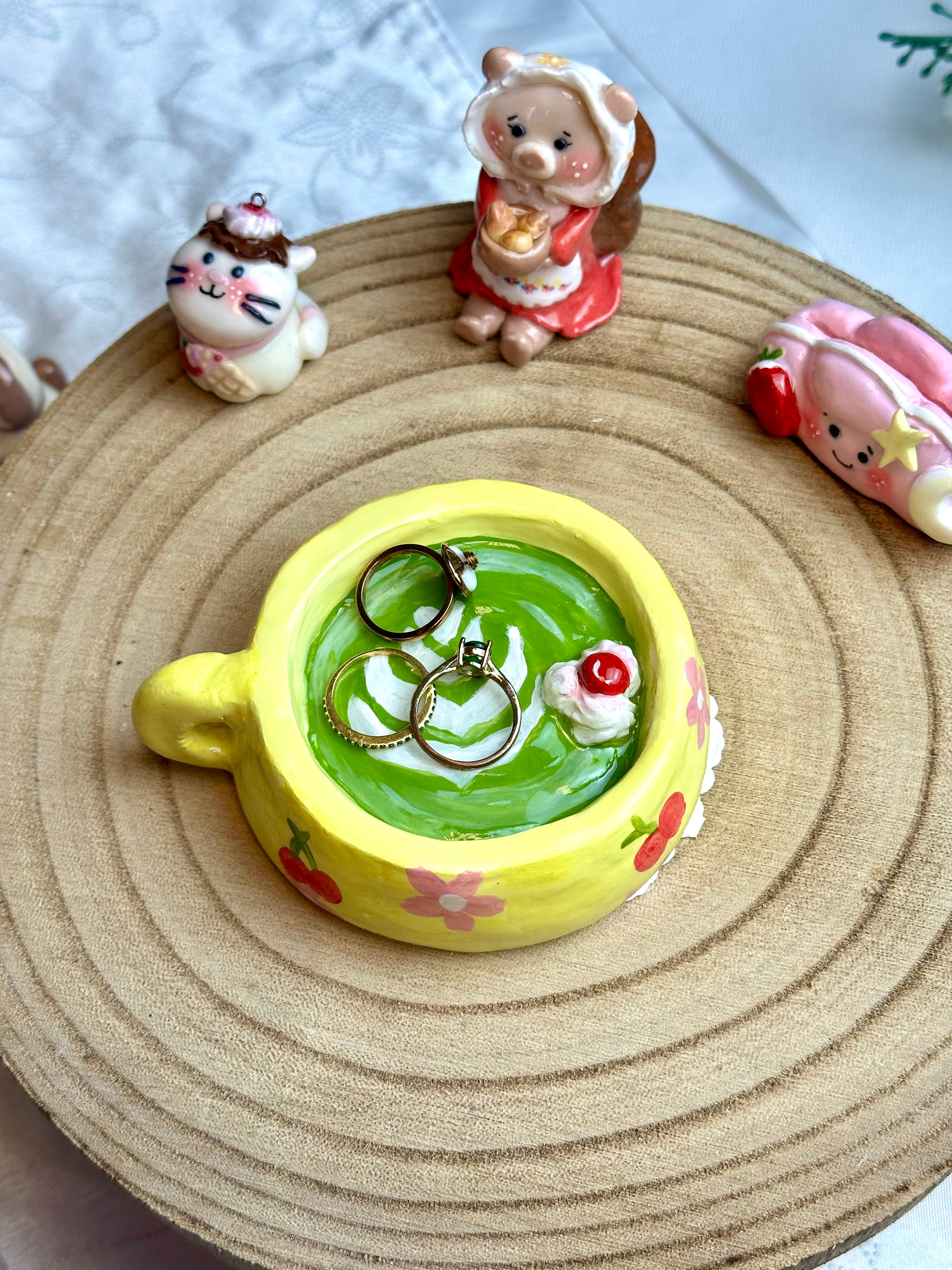 Yellow buttercup matcha ring holder cup with green beverage and two rings on a woven mat with small decorative figures.