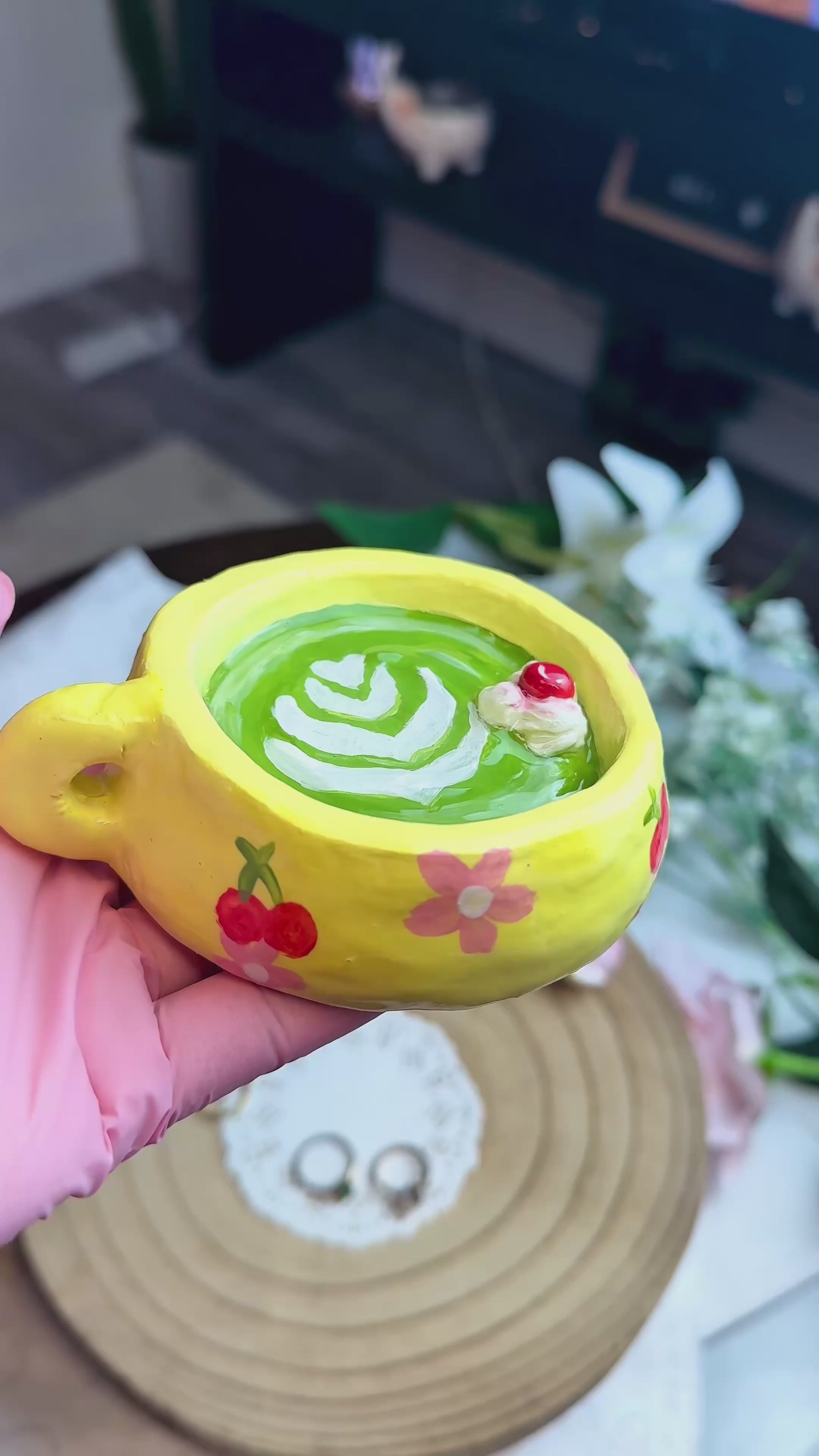 Video of Yellow buttercup matcha ring holder cup with green beverage and two rings on a woven mat with small decorative figures.
